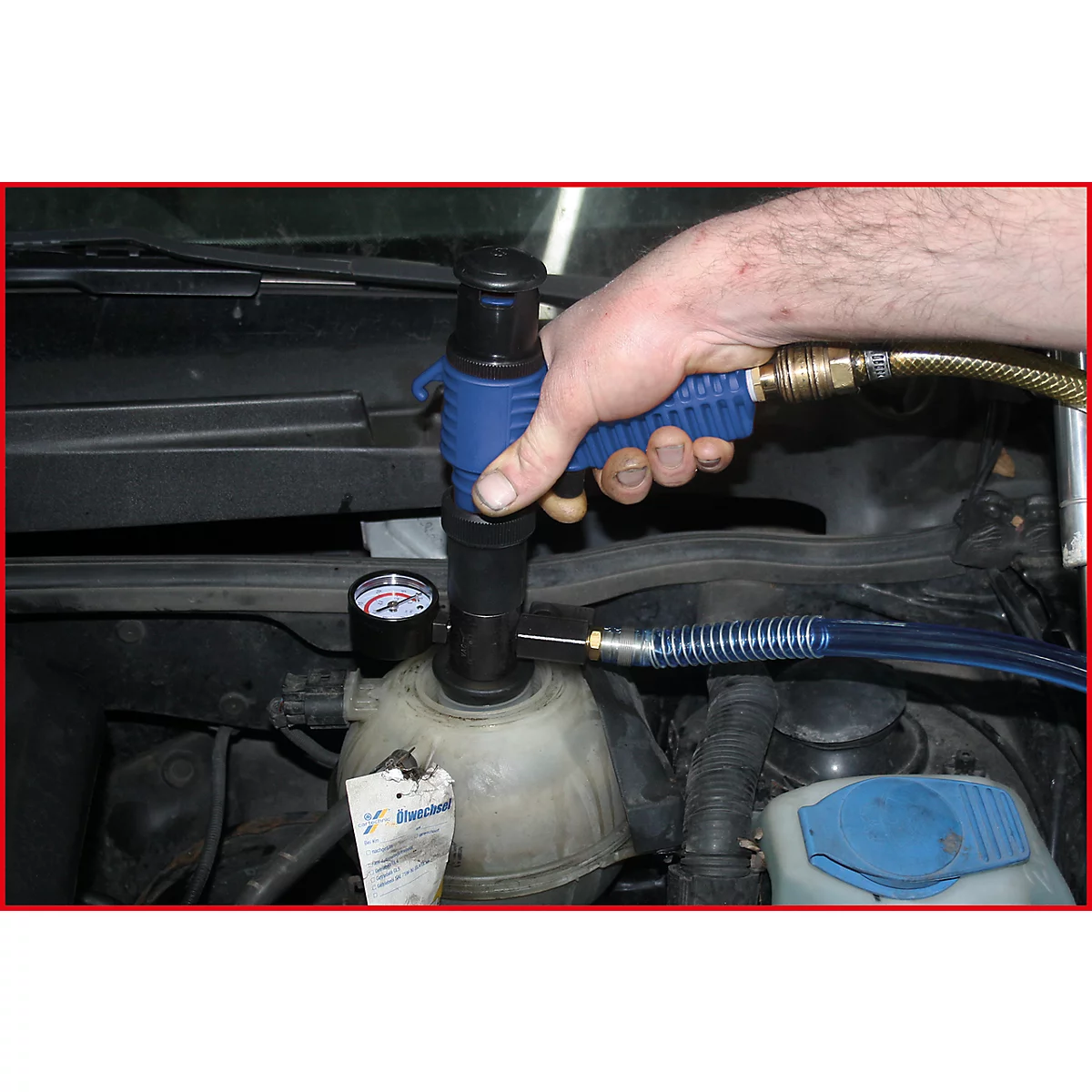 Mann befüllt Kühler eines Autos mit einem Werkzeug. Manometer und Schlauch sichtbar.